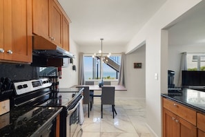 A kitchen with wooden cabinets, a stove, and a dining area with a view. - Charming 2BR Coastal Getaway in Pacifica (Pacifica)