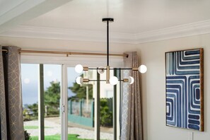 Ein Zimmer mit einer Deckenleuchte, einer Schiebetür zu einem Außenbereich und einem gerahmten abstrakten Gemälde an der Wand.