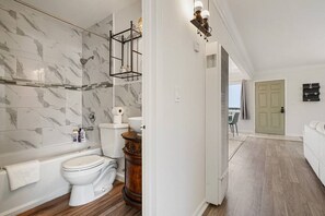 Un baño con pared de mármol, inodoro, bañera y mueble de madera.