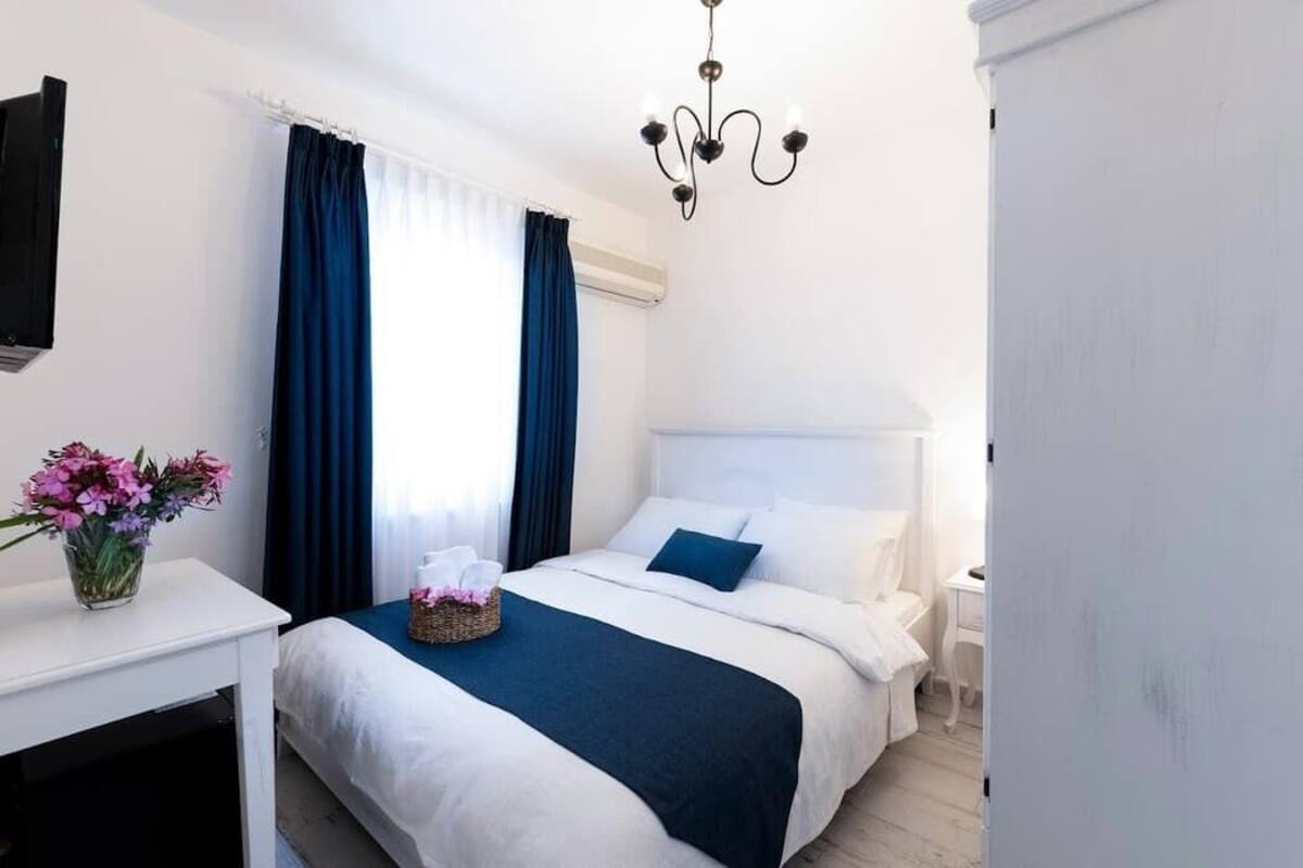 A hotel room with a bed, a bedside table with a vase of flowers, a nightstand, a TV, and a chandelier.