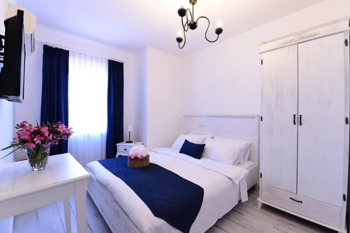 A hotel room with a bed, a nightstand, a TV, a wardrobe, and a window with curtains.