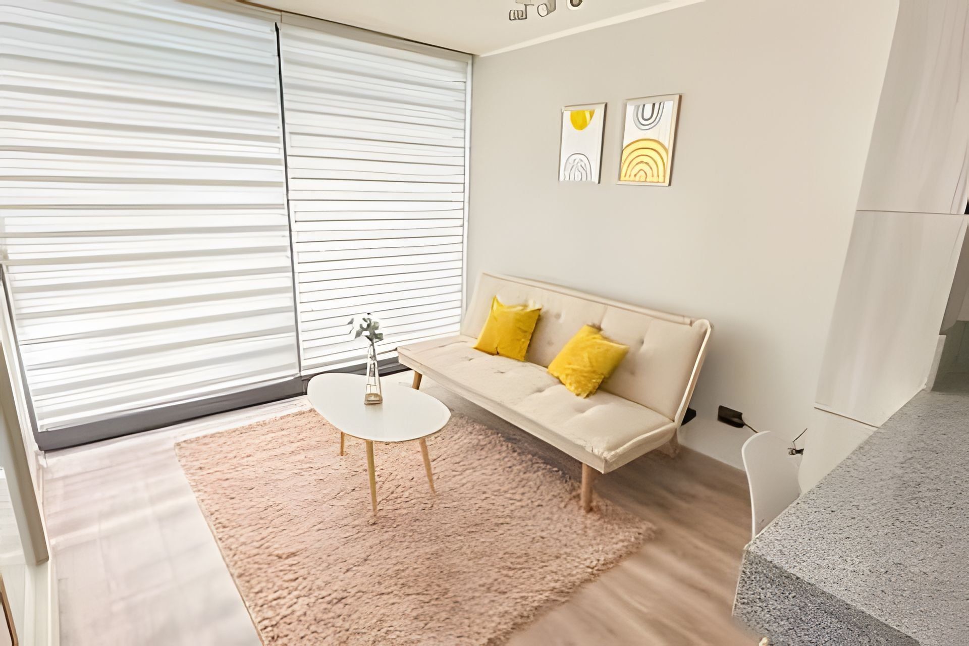 A modern living room with a sofa, a small table, and a large window with blinds.
