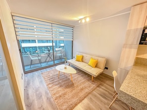 A modern living room with a sofa, a small round table, and a view through a sliding glass door to an outdoor balcony. - Depto acogedor cercano a metro y centro (Santiago)