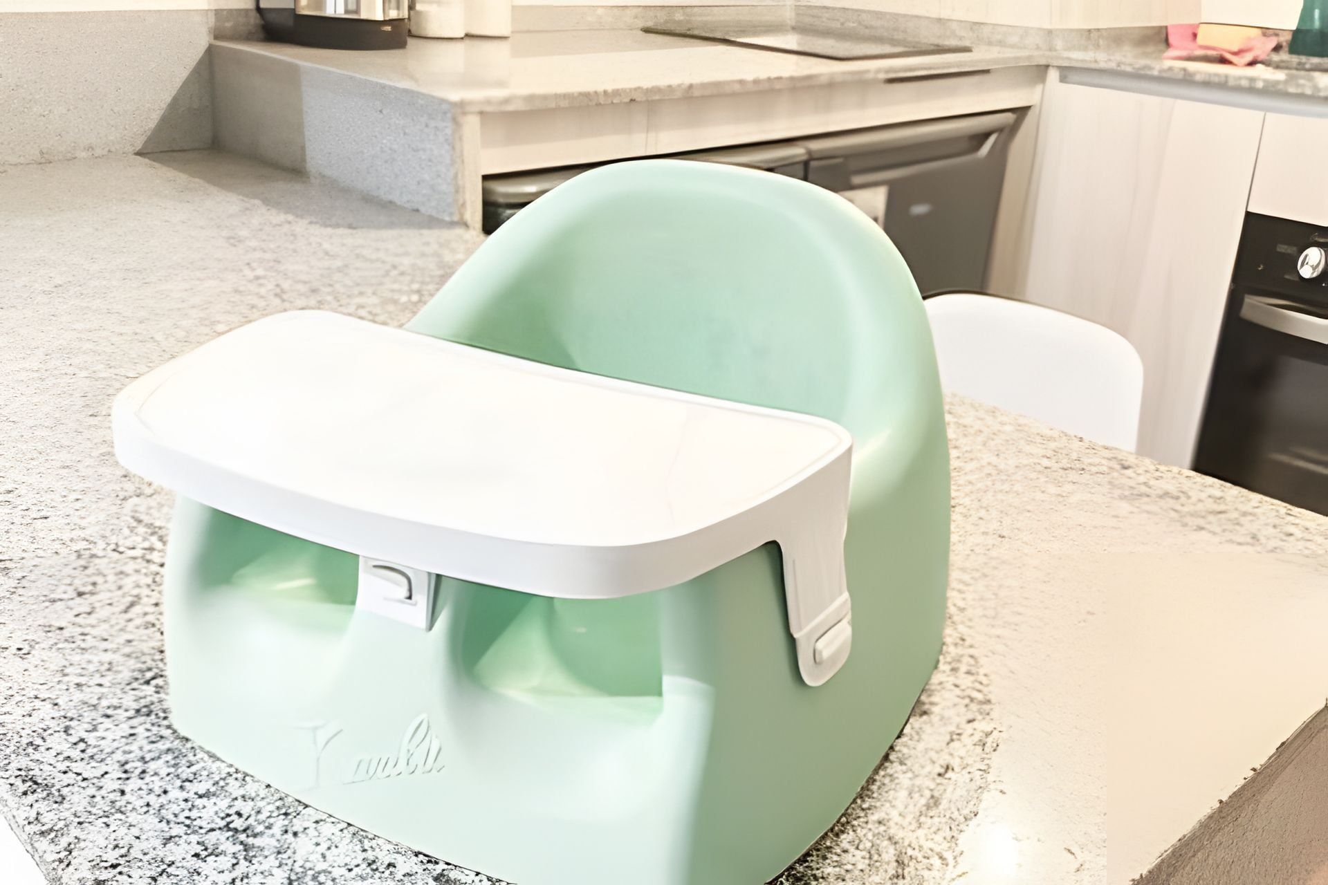 A kitchen with a green and white baby high chair on a granite countertop.