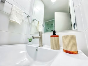 A bathroom with a white sink, a mirror, a shower, and a small potted plant. - Depto acogedor cercano a metro y centro (Santiago)