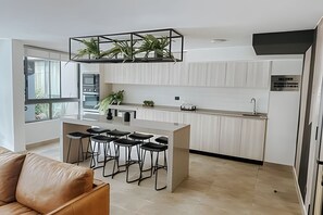 A modern kitchen with a central island, bar stools, and a hanging plant. - Depto acogedor cercano a metro y centro (Santiago)