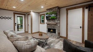 A living room with a stone fireplace, a television mounted on the wall, and a wooden ceiling. - Your Modern Creekside Retreat with Resort Perks! Modern 2bdrm + Open LoftTrundle (Ellijay)