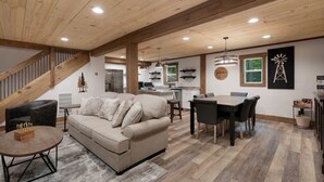 A spacious living area with a wooden ceiling, a sofa, a dining table, and a kitchen in the background. - Your Modern Creekside Retreat with Resort Perks! Modern 2bdrm + Open LoftTrundle (Ellijay)