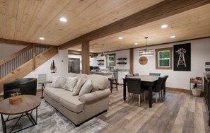A spacious living area with a wooden ceiling, a sofa, a dining table, and a kitchen in the background. - Your Modern Creekside Retreat with Resort Perks! Modern 2bdrm + Open LoftTrundle (Ellijay)