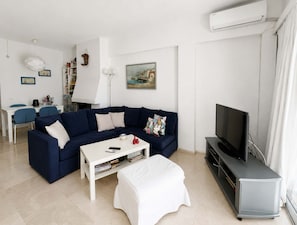 Ein Wohnzimmer mit einem dunkelblauen Sofa, einem weißen Couchtisch, einem TV-Schrank und einem Gemälde an der Wand.