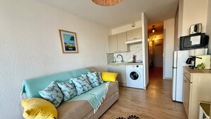 Ein kompakter Wohnraum mit Sofa, Waschmaschine, Küchenzeile und Essbereich.