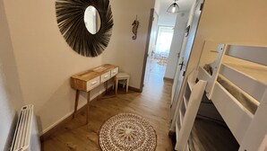 Ein Flur mit einem runden Spiegel, einem Holzkonsolentisch, einem kleinen Hocker, einem gemusterten Teppich und einem Etagenbett.