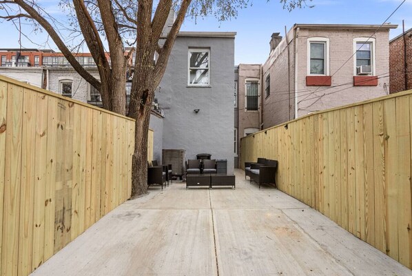 A narrow courtyard with a grey building, wooden fences, and outdoor furniture.