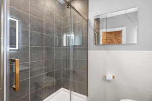 Een moderne badkamer met een douchecabine van glas, een wit toilet en een spiegel met een achterwand van baksteen.