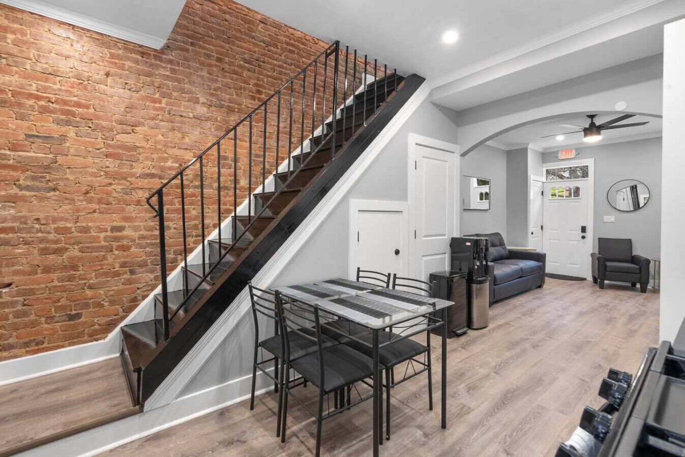 A staircase with a brick wall, a dining area with a table and chairs, and a living area with a sofa and a coffee machine.