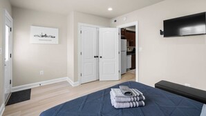A bedroom with a bed, a TV mounted on the wall, and a door leading to a kitchen. - Modern NoMa Retreat | 2BR Near UnionMarket & Metro (Washington)