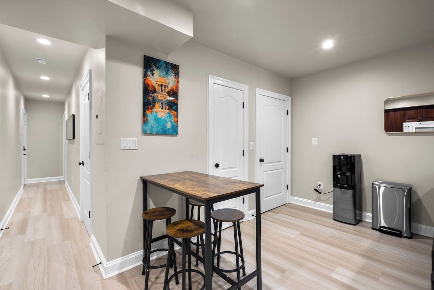 A kitchen with a wooden table, two bar stools, a refrigerator, and a water dispenser.