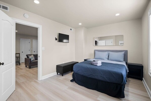 A bedroom with a bed, bedside tables, a TV, a mirror, and a door leading to another room. - Modern NoMa Retreat | 2BR Near UnionMarket & Metro (Washington)