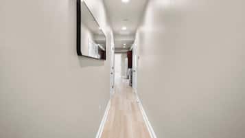 A modern hallway with a wooden floor, a large mirror on the left wall, and recessed ceiling lighting.