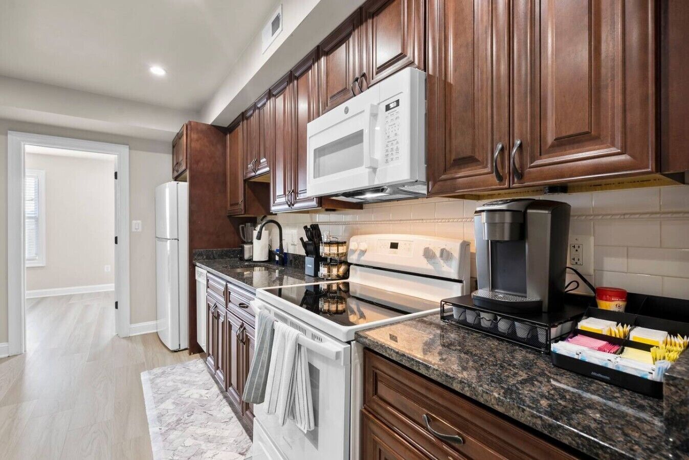A modern kitchen with wooden cabinets, a white microwave, a stove, and a coffee maker.
