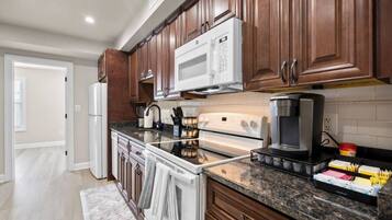A modern kitchen with wooden cabinets, a white microwave, a stove, and a coffee maker.