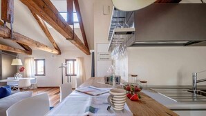Moderni keittiö, jossa on puupalkkeja, ruokailutila puupöydän kera sekä näkymä olohuoneeseen.