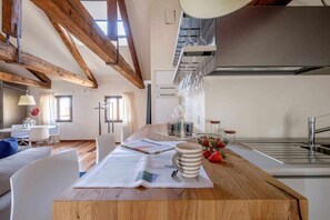 Eine moderne Küche mit Holzbalken, ein Essbereich mit einem Holztisch und Blick zum Wohnzimmer.