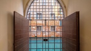 Kapea käytävä, jonka päässä on metallinen portti, joka johtaa sisäpihalle, jossa on tiilimuuri ja ikkuna.