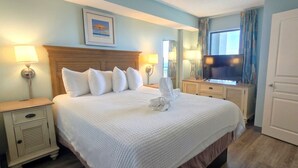 Una habitación de hotel con una cama grande, dos mesitas de noche, un televisor y una ventana con cortinas.