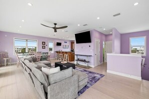 Ein geräumiges Wohnzimmer mit einer großen Couch, einem an der Wand montierten Fernseher und einem Deckenventilator.