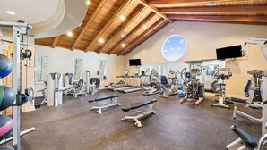 Et fitnessrum med forskellig træningsudstyr, træloft og et stort vindue.