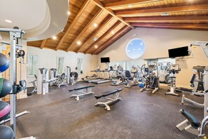 Ein Fitnessraum mit unterschiedlichen Trainingsgeräten, einer Holzbalkendecke und einem großen Fenster.