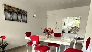 Un coin repas avec une table blanche et des chaises rouges, une plante en pot et un tableau accroché au mur.