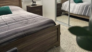 Une chambre à coucher avec un lit, une table de chevet, une lampe, un miroir et une fenêtre avec des stores.