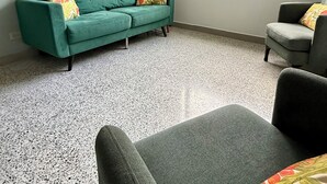Une pièce avec un canapé vert, un fauteuil gris, une lampe sur pied et un ventilateur de plafond.