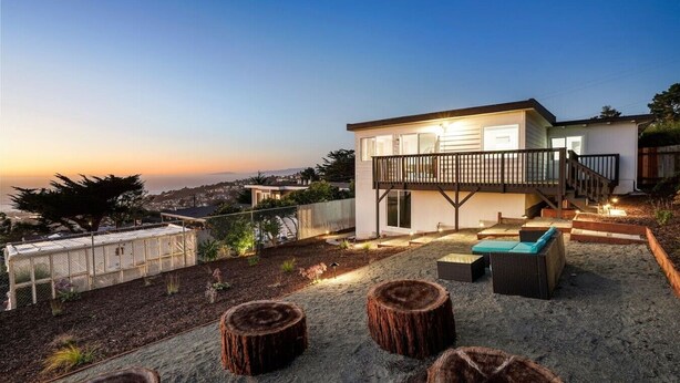 Una casa moderna con balcón, mobiliario exterior y vistas a la ciudad al atardecer.