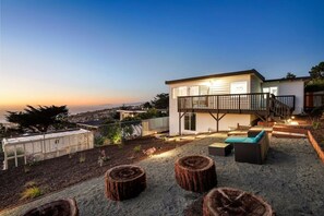 A modern house with a balcony, outdoor seating, and a view of the city at sunset.
