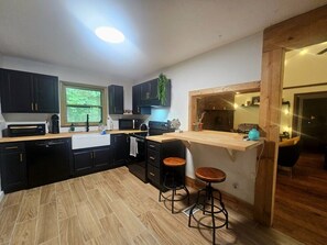 Une cuisine moderne avec des meubles de couleur noire, un plan de travail en bois et deux tabourets.