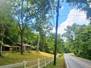 Une route de campagne bordée d’une clôture blanche, d’arbres et d’une maison dotée d’un porche.