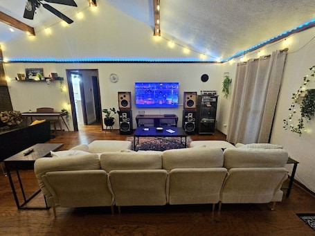 A living room with a sectional sofa, a coffee table, a TV, and two speakers.. The Timber & Tune Retreat: 3BR Woodland Oasis | Huge Rolling Yard | 15 Min to Ryman