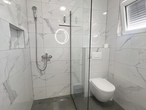 Ein modernes Badezimmer mit einer gläsernen Duschkabine, einer Toilette und Wänden mit Marmor-Optik.