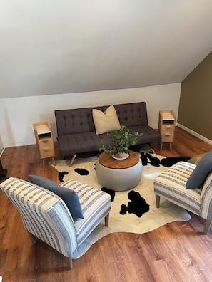 A living room with a sofa, two patterned armchairs, a round coffee table with a plant, and a cowhide rug. - Lovely 4-bedroom house in Teaneck - 3 mins walk to bus, 20 mins drive NYC. (Teaneck)