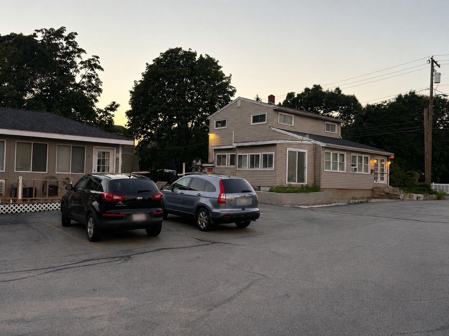 Un parking où sont garées deux voitures devant une rangée de maisons de plain-pied, protégées par une clôture en piquets.