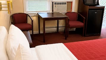 Habitación de hotel con cama, una mesa, dos sillas, una lámpara, equipo de aire acondicionado, microondas y refrigerador.