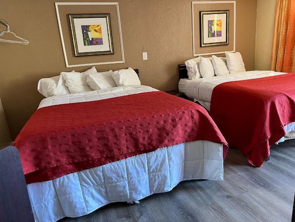 Two double beds with red and white bedding, framed artwork on the walls, and a wooden floor.