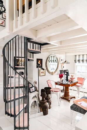 Ein modernes Interieur mit einer Wendeltreppe, einem Essbereich mit Holztisch und -stühlen sowie einem großen Spiegel an der Wand.