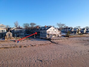 Ein Küstenanwesen mit einem großen Haus, einem hölzernen Steg und einem Sandstrand.
