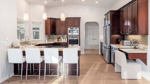 A modern kitchen with a central island, bar stools, stainless steel appliances, and pendant lighting. - Massive Villa +Casita +Waterslide + Spa + VBall (Cave Creek)