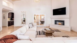A spacious living room with a white sofa, a fireplace, a television, and a chandelier. - Massive Villa +Casita +Waterslide + Spa + VBall (Cave Creek)