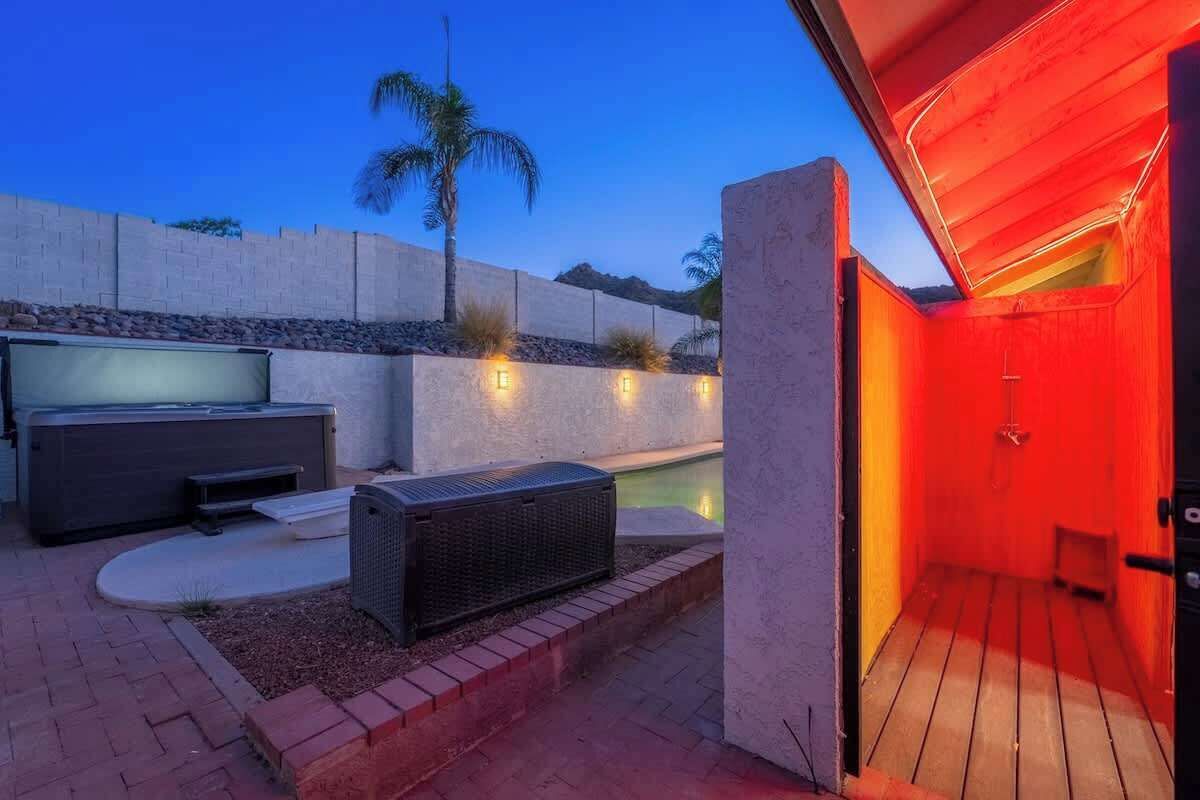 Um pátio externo com piscina, área de estar coberta e entrada iluminada em vermelho.
